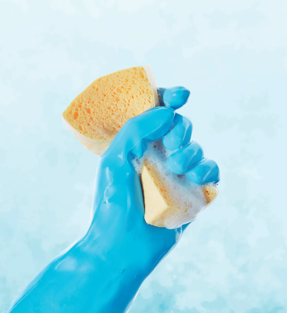 Mano con guante azul sosteniendo una esponja de celulosa